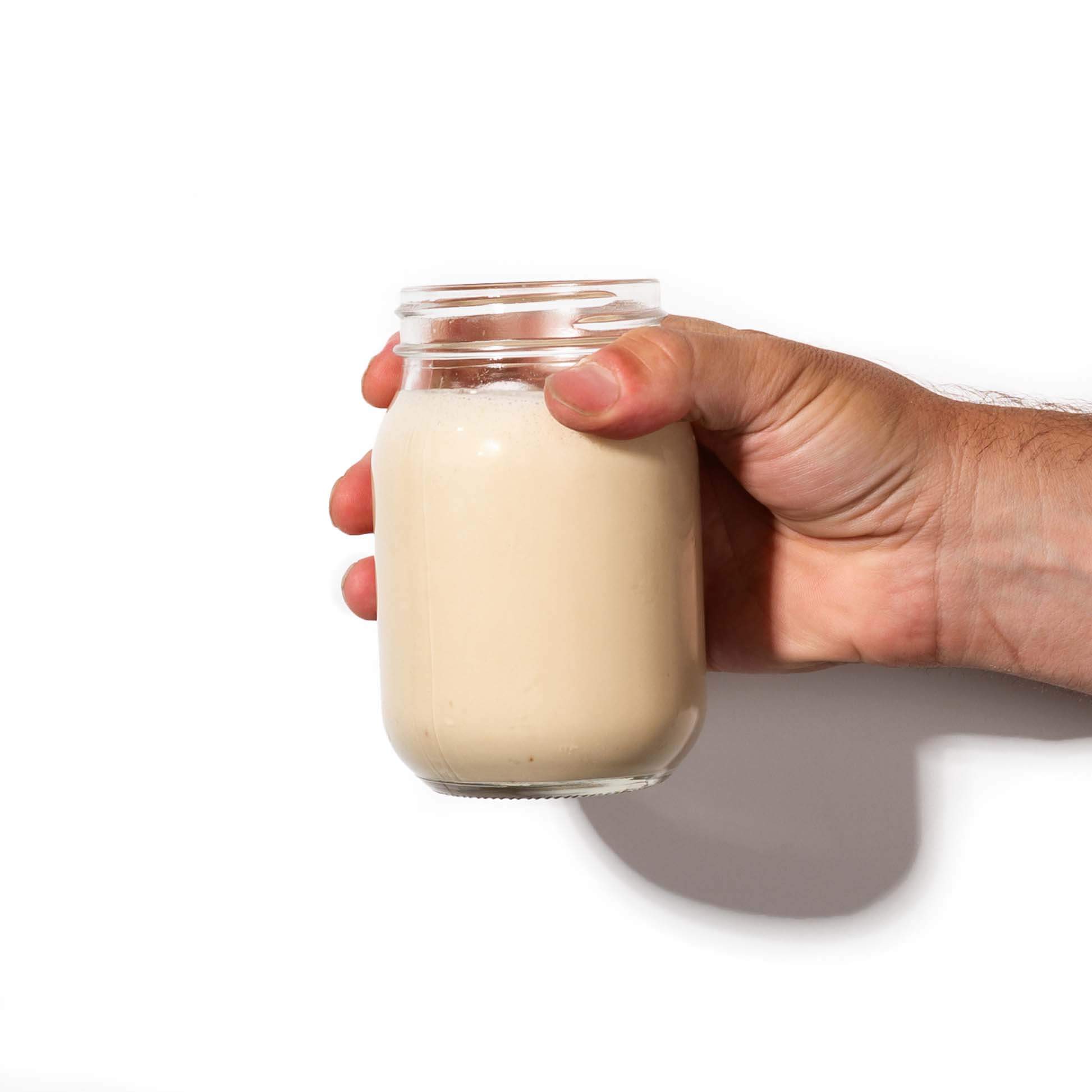 Hand holding a jar filled with organic plant protein powder drink.